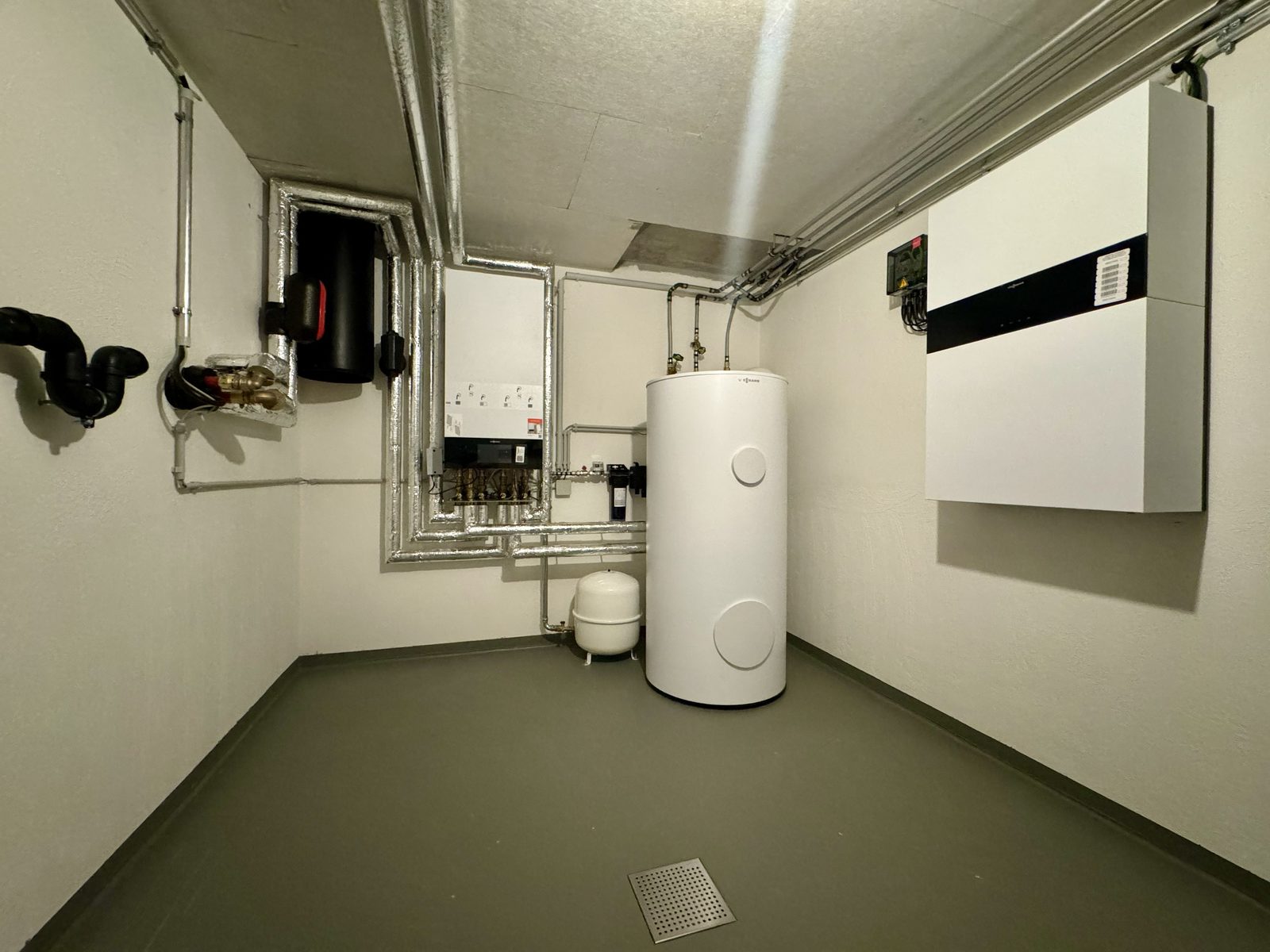 Heizungsraum mit Warmwasserspeicher und Wärmepumpen-Regelung an der Wand
